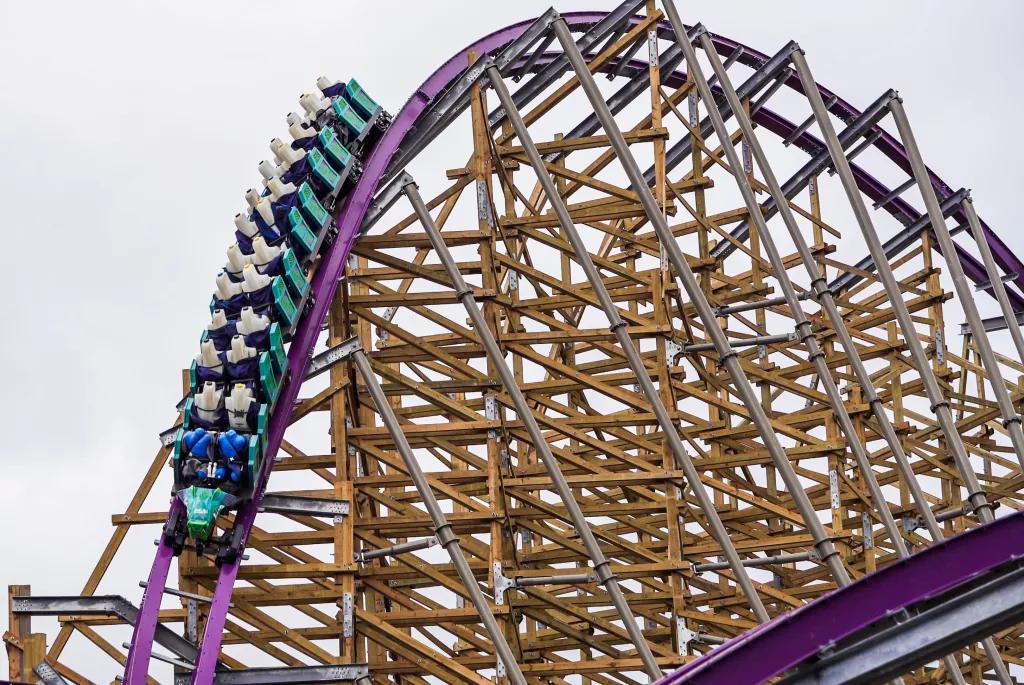 Iron Gwazi A teal coloured rollercoaster car going down a slope on a hybrid wood and steel coaster