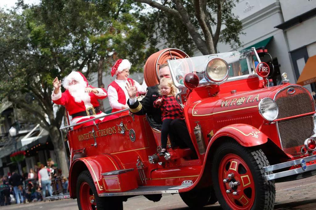 Winter Garden Christmas Parade A man and child riding in a red old-fashioned fire truck with Santa and Mrs Clause in the back