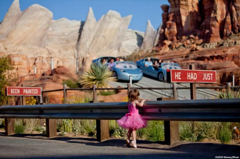 Cars Land A young girl in a pink tutu watching two ride vehicles go past designed to look like cars from the Pixar movie Cars