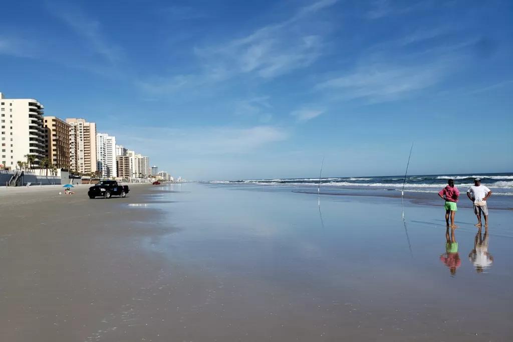 Daytona Beach People standing on the shore of a quiet beach in front of a bright blue sky