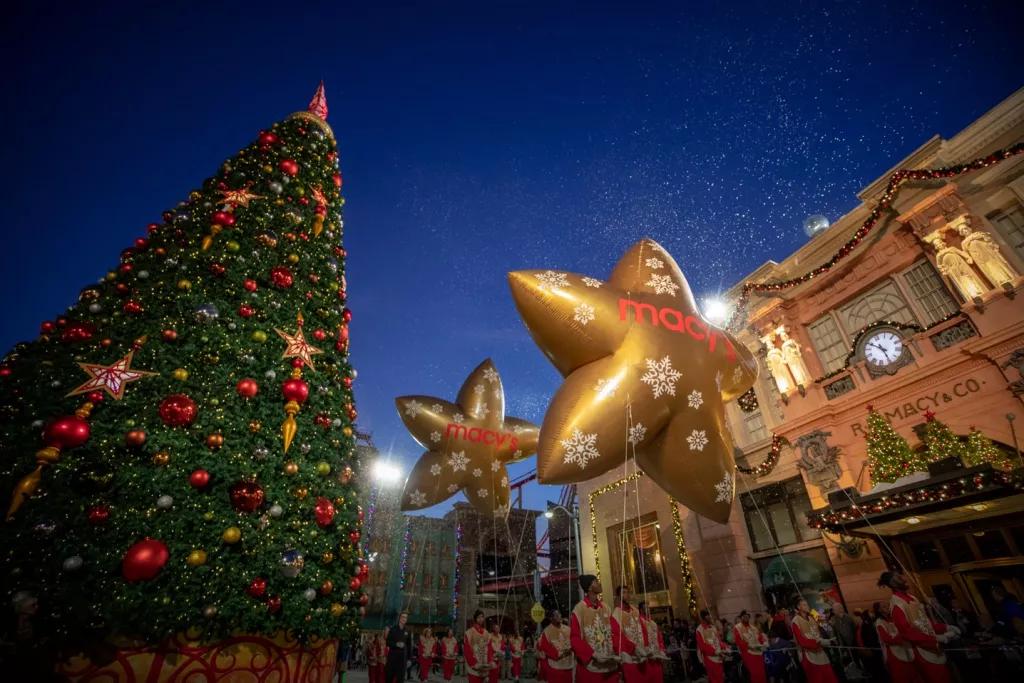 Christmas at Universal Orlando Large gold star-shaped balloons being carried past a tall Christmas tree