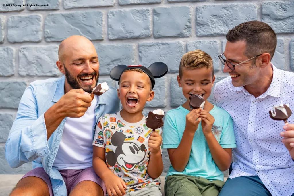 Mickey Bars Two men and two young boys sat down eating chocolate covered ice cream
