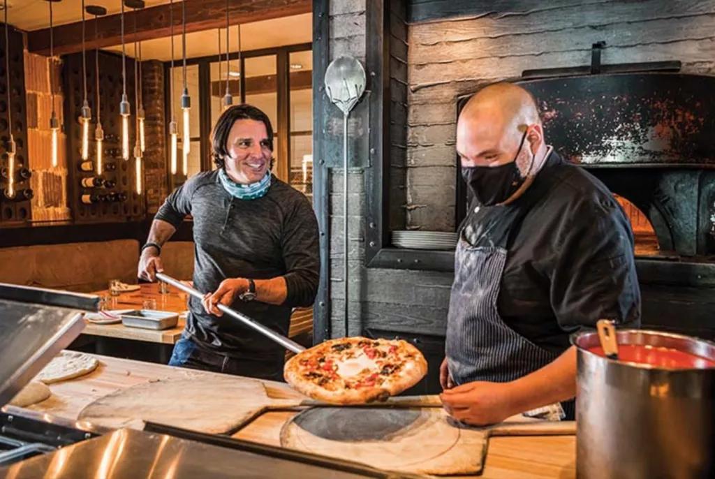 Prato Pizza Two men serving a pizza onto a wooden board
