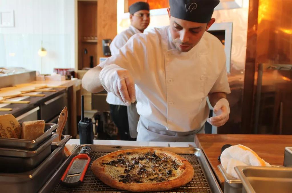 Wolfgang Puck Pizza A chef sprinkling cheese onto a pizza