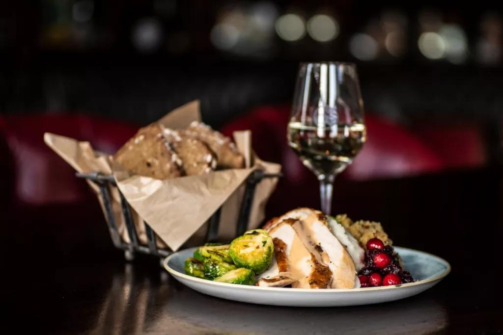 Christmas Dinner at Raglan Road A plate of turkey, brussel sprouts, stuffing and cranberry sauce in front of a basket of bread and a glass of wine