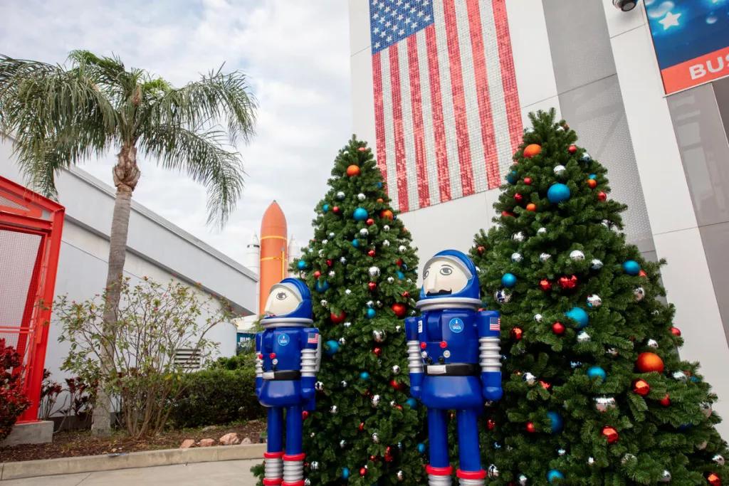Space-Themed Christmas Decor Large astronaut themed nutcrackers in front of Christmas trees and a building with an American flag