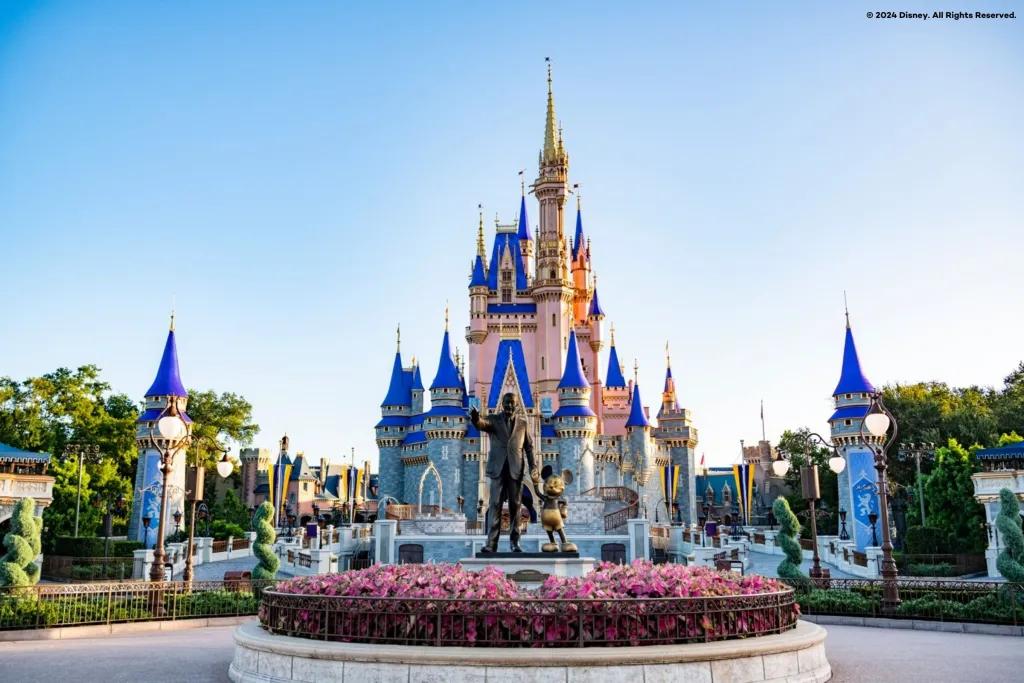Cinderella Castle A large pink and blue castle in front of a clear blue sky. A statue of Walt Disney and Mickey Mouse is in the foreground