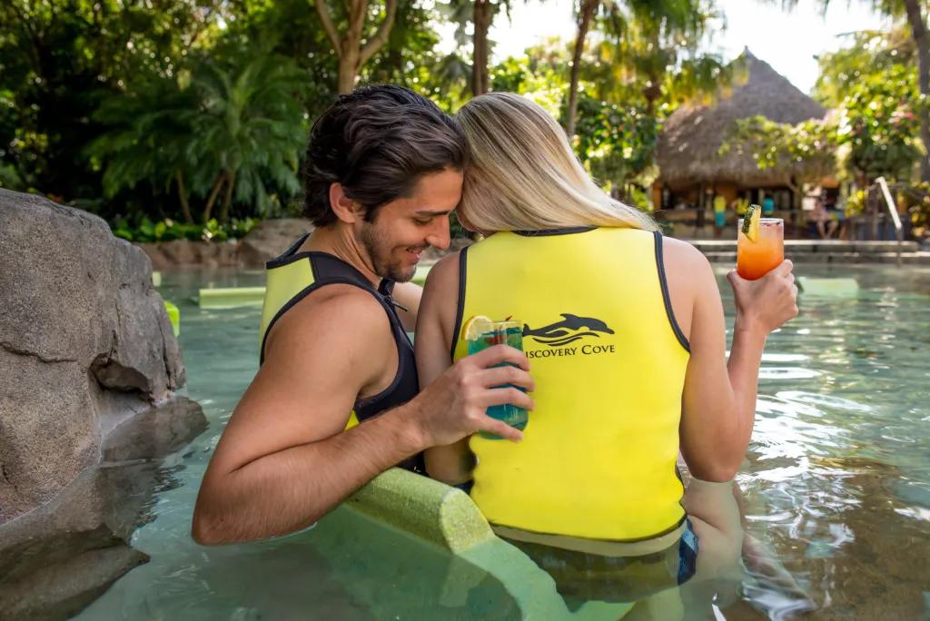 Discovery Cove A couple sitting in shallow water holding cocktails and leaning in to each other