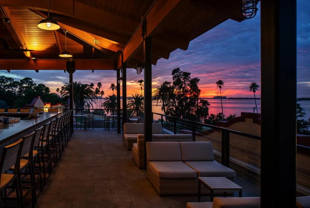 Al Fresco Dining in Orlando An outdoor dining terrace with low tables and bar seating. In the background is a blue and pink sunset over a beach