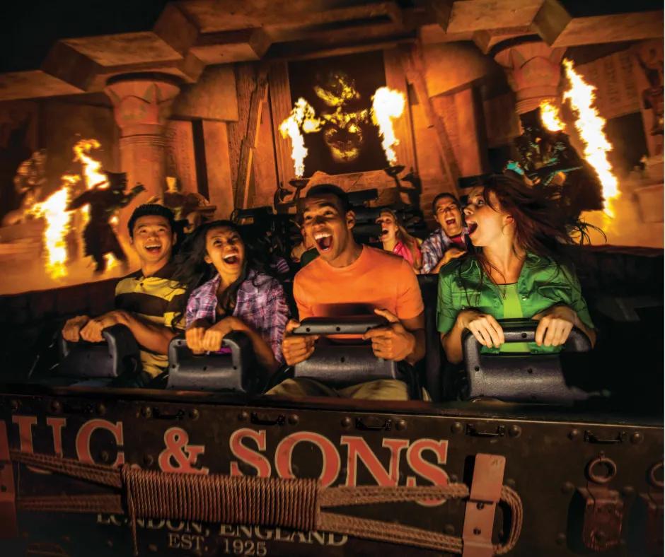 Revenge of the Mummy in Universal Studios Florida People sat in the coaster car with four in the front clutching the lap bars and screaming. Fire pyrotechnics and animatronic mummy's surrounding them and a large projection of a mummy face behind them.