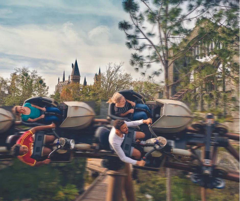 Hagrid's Magical Creatures Motorbike Adventure Four guests turned to the side on a coaster, sat in carts shaped like a motorbike, zooming through trees in front of the brown Hogwarts castle