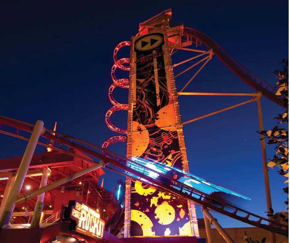 Hollywood Rip Ride Rockit Red and yellow roller coaster at night with 90 degree chain lift up high which leads into steep drop and a rollercoaster car with multicoloured lighting on track