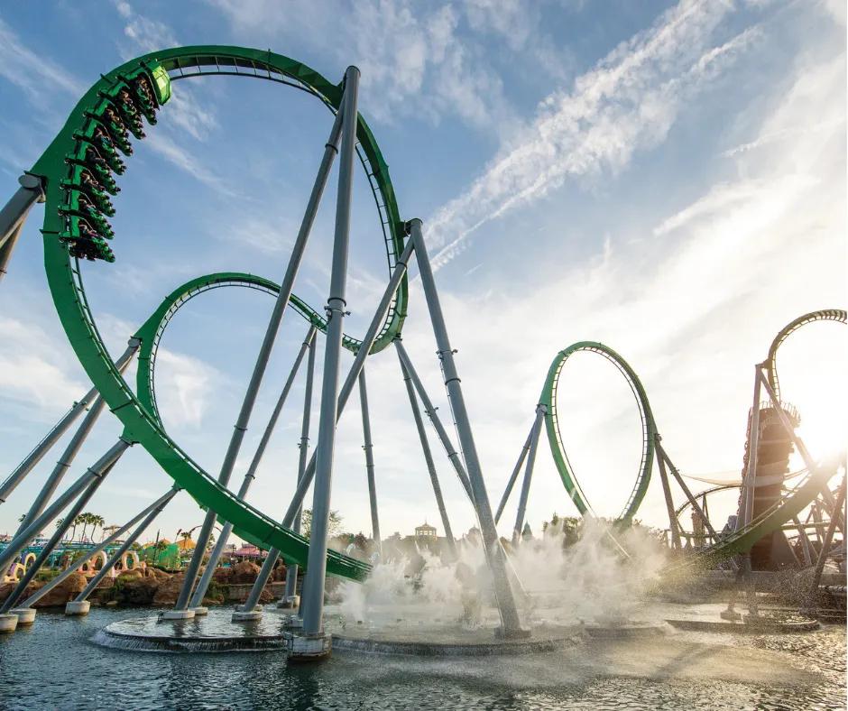 The Incredible Hulk Coaster at Universal's Island of Adventure Giant green rollercoaster with two vertical loops and a car in motion on track diving towards lake surrounded by mist