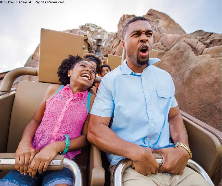 Expedition Everest at Animal Kingdom Theme Park A young girl and an older man sat together on the ride with the girl in a bright pink top leaning over smiling towards the man who is grabbing the lap restraints and screaming