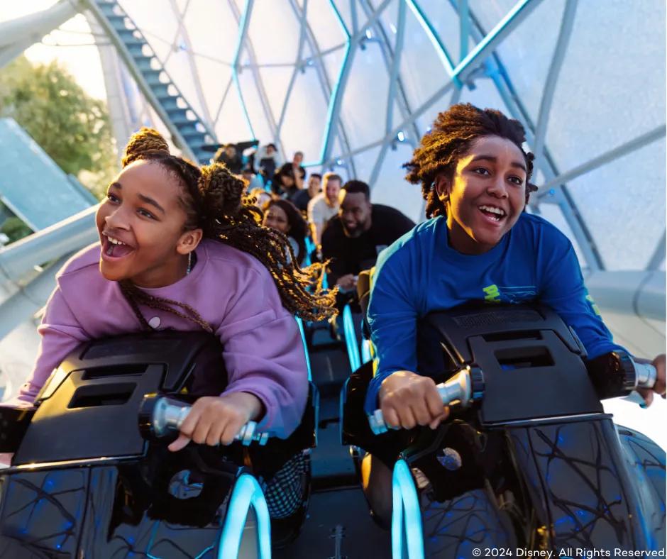 Guests riding TRON Lightcycle/Run Two guests smiling as they are launched, sat on bike shaped vehicle riding TRON Lightcycle/Run