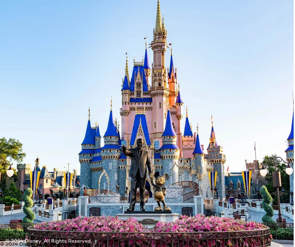 Cinderella's Castle in the Magic Kingdom Park Statue of Walt Disney holding hands with Mickey Mouse in front of large pink and blue castle