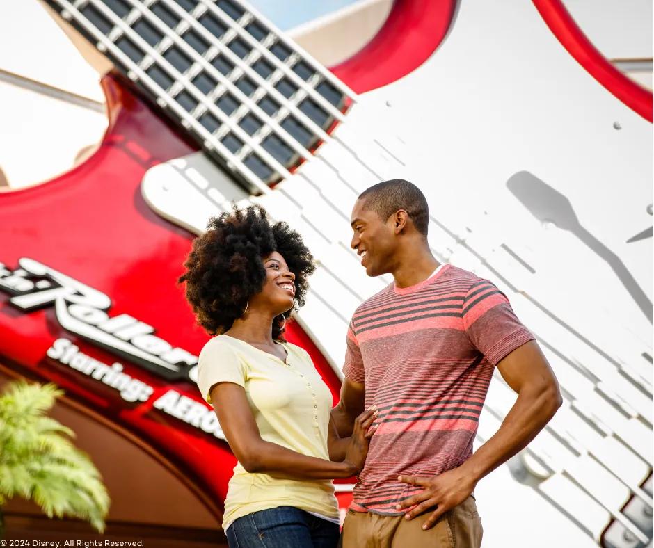 Rock 'n' Roller Coaster Starring Aerosmith in Disney's Hollywood Studios Couple looking at one another smiling, stood in front of a giant red guitar sign at the front of the Rock 'n' Roller Coaster ride with the ride title written on the bottom left of the guitar.
