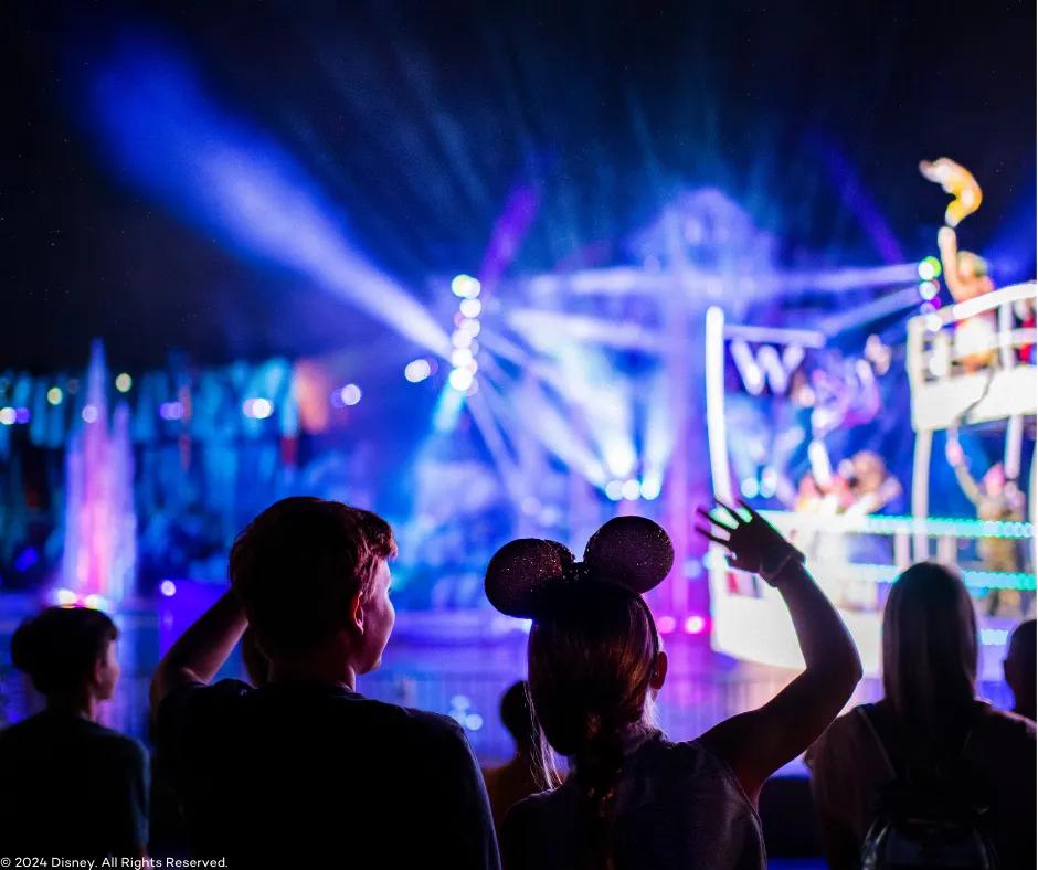 Fantasmic! at Disney's Hollywood Studios Behind two children watching Fantasmic! One girl wearing mickey ears and one boy with one of each of their hands in the air. In the blurry background there are multicoloured lasers shining, purple and blue lighting, fountains and the front of a white ferry boat holding Disney characters.