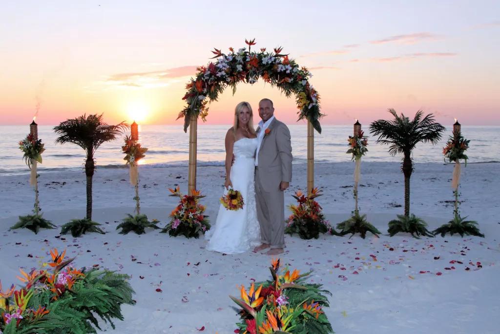Niceville Beach Wedding A bride and groom standing on a beach at sunset in front of a floral wedding arch