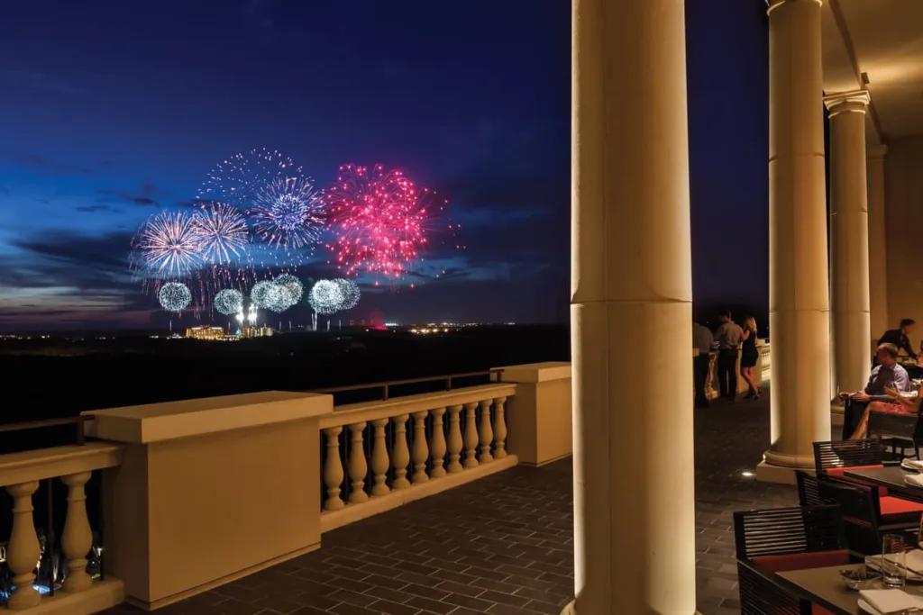 People standing on a gran balcony watching brightly coloured fireworks in the distance