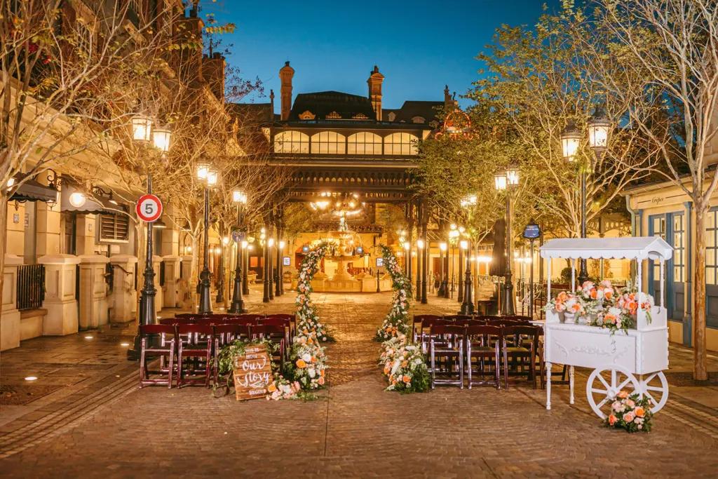 Place de Remy in EPCOT Rows of benches and a floral wedding arch in front of a facade of Paris at dawn