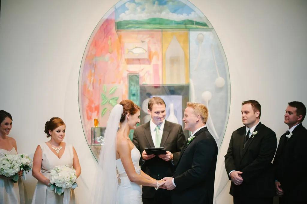 Orlando Museum of Art A bride and groom next to their bridesmaids and groomsmen getting married in front of a large oval-shaped piece of art