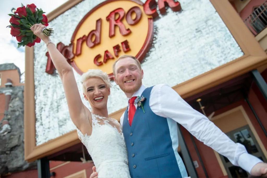 Hard Rock Cafe Wedding A bride holding her bouquet in the air with her arm around her groom. They are posing in front of the Hard Rock Cafe sign