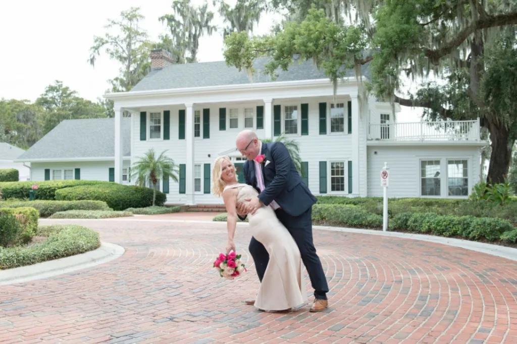 Cypress Grove A groom dipping his bride over his knee. They are posing in front of a white American country house.