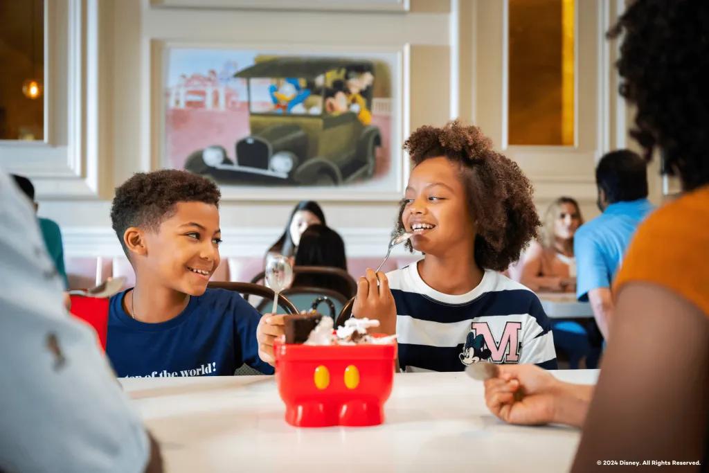 Beaches and Cream Soda Shop Two young children smiling at each other while eating an ice-cream sundae