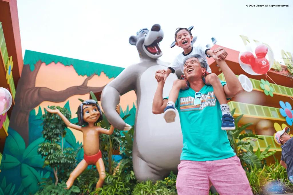 Disney's Pop Century Resort A man with a young boy on his shoulders walking next to a large statue of Mowgli and Baloo from The Jungle Book