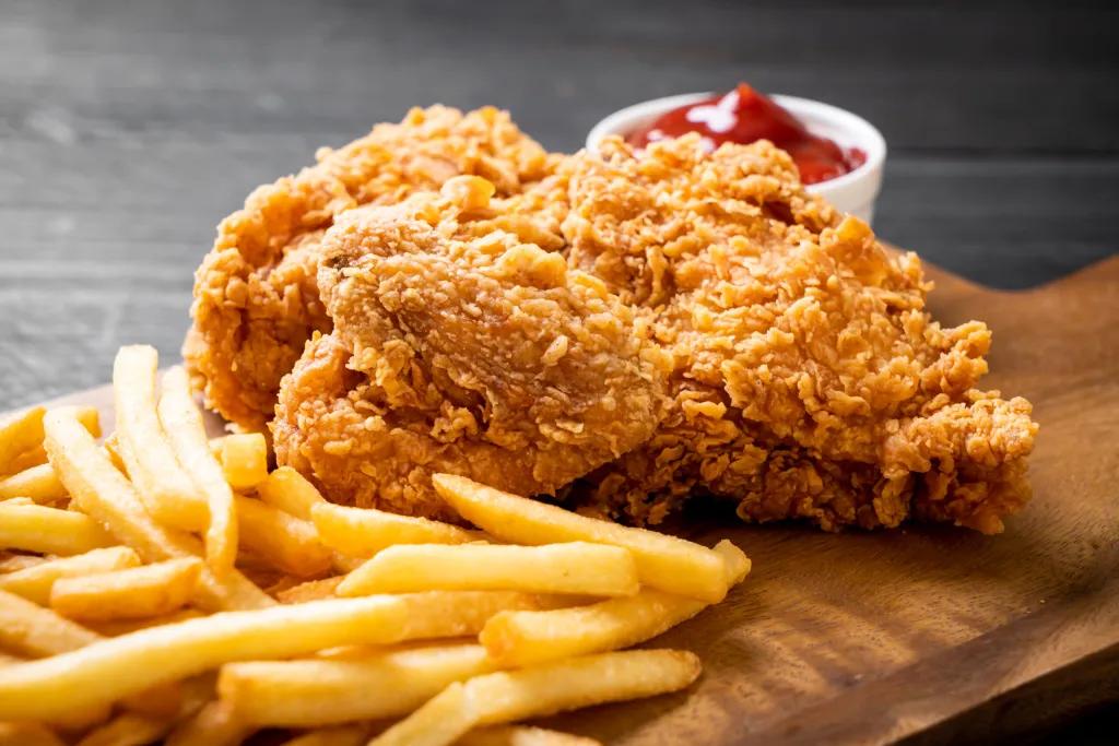 Crispy fried chicken dish Crispy piece of fried chicken and fries on a wooden board next there is a white circular pot of ketchup.