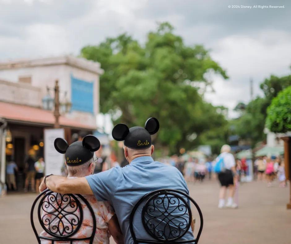 Ein älteres Paar mit Micky Ohren sitzt auf einer Bank Ein älteres Paar mit Micky Ohren sitzt auf einer Bank im Disney Park