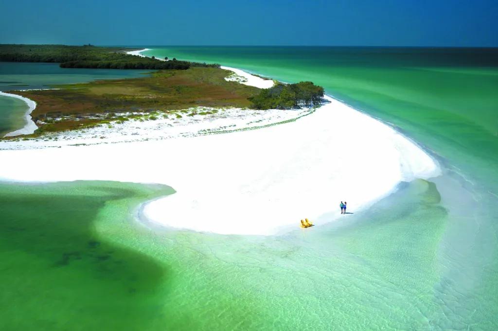 Caladesi Island Two yellow deck chairs and a couple walking along white sandy beach of deserted island.