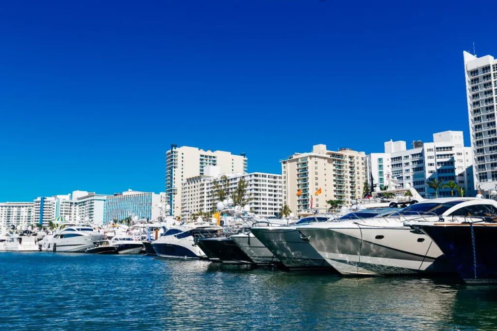 Miami luxury Yachts and boats docked in harbour with the Miami skyline in the background, lots of tall buildings.