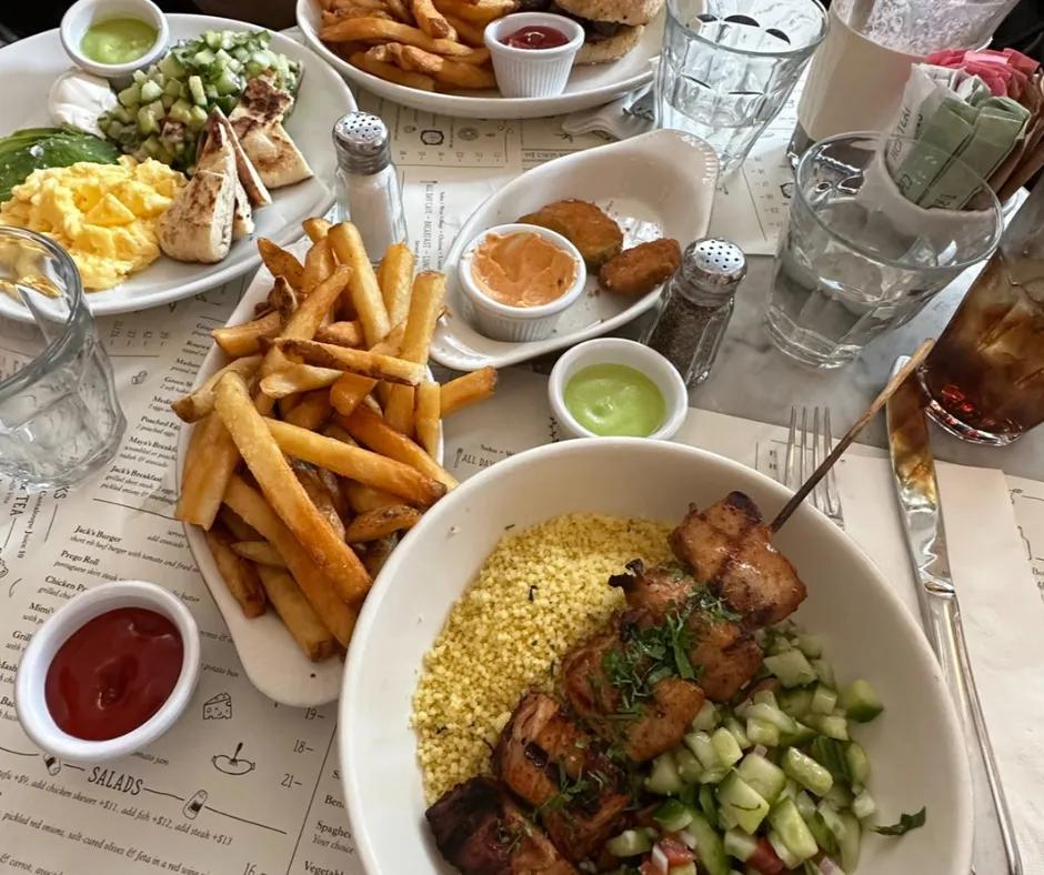 Jack's Wife Freda, New York City Table with a lot of food on it. There are white bowls with chips, fried pickles, chicken kebab, salad and eggs with avocado.