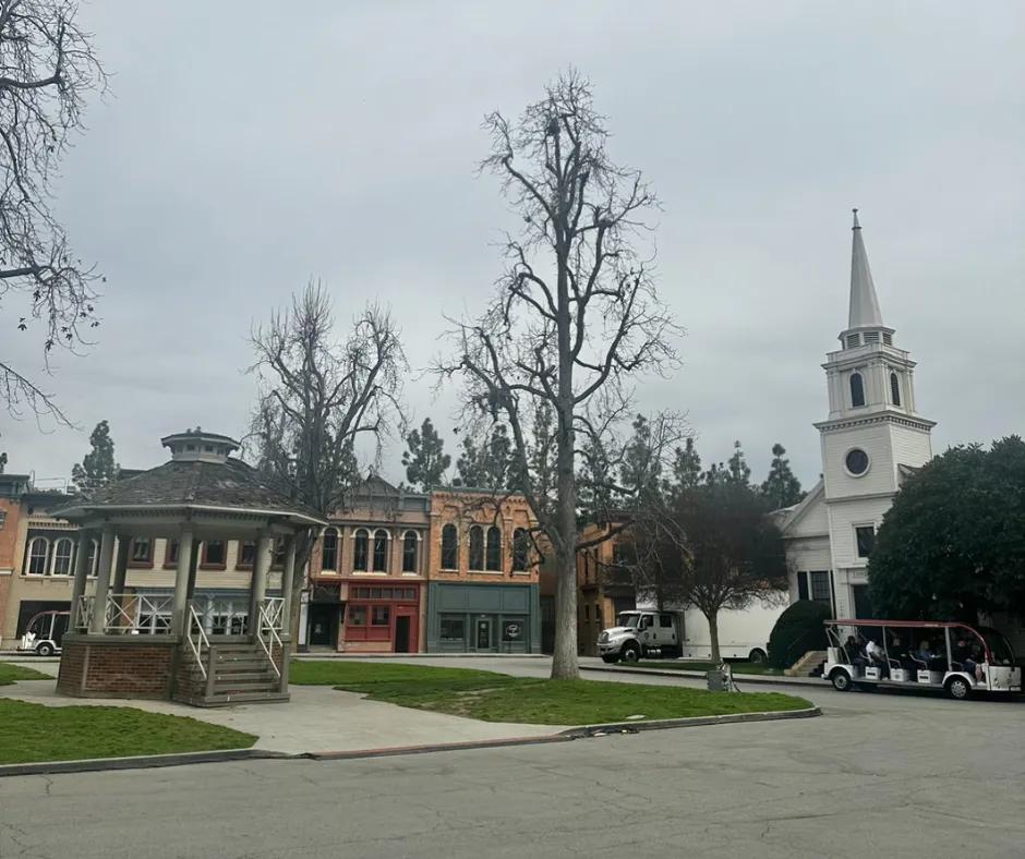 Pretty Little Liars set White gazebo to the left, with buildings of varying colours behind such as red and dark blue store fronts below. A large white lorry is next to the white church with pointed roof and circular windows.