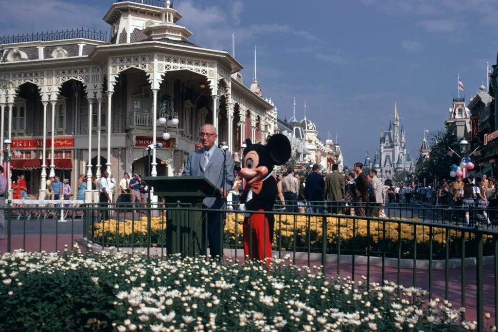 Dedication Ceremony at Walt Disney World Resort in Florida Old image of main street and Cinderella's Castle and in front Mickey is stood with Walt Disney as he delivers a speech.