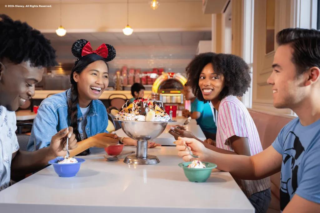 Beaches and Cream Soda Shop A group of friends sat round a table in a diner eating a giant ice cream sundae