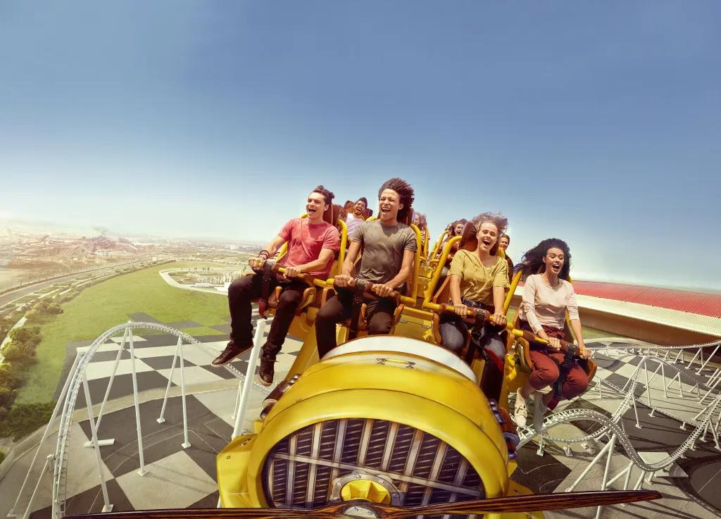 Flying Aces White rollercoaster track on black and white floor with yellow coaster car and four people screaming and smiling whilst clinging onto the lap bars.