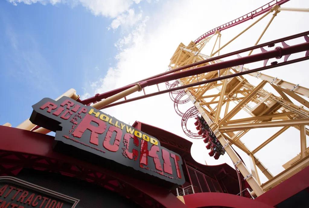 Hollywood Rip Ride Rockit Rollercoaster red cart heading up a vertical chain lift surrounded by circular steel arches, almost about to drop down the steep red and yellow track. There is a black sign with red and yellow text saying "Hollywood Rip Ride Rockit"