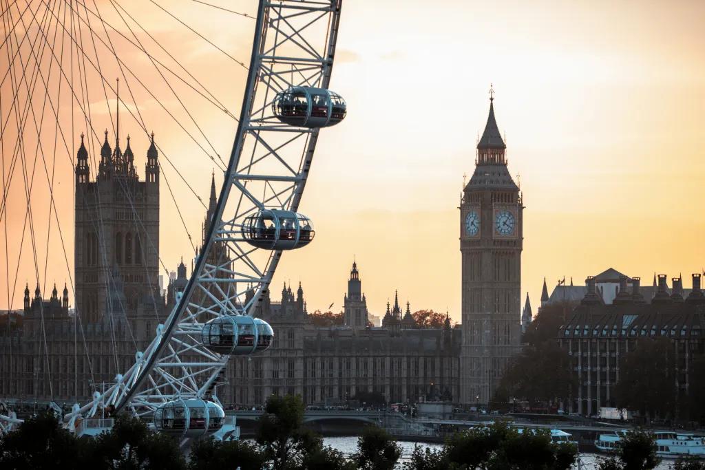 The London Eye The London eye, a circular ferris wheel with large glass pods on, in front of a large ancient building and clock tower known as the Houses of Parliament and Big Ben.