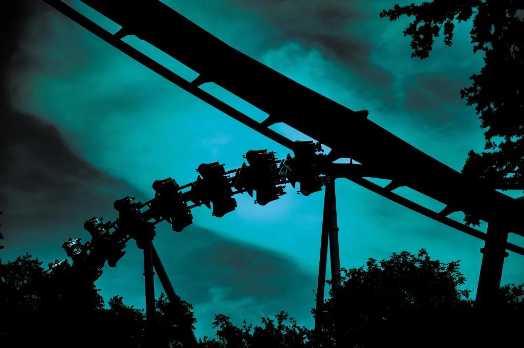Manta during Howl-O-Scream Dark night sky with streaks of turquoise light which outline the silhouette of manta roller coaster flying through track.