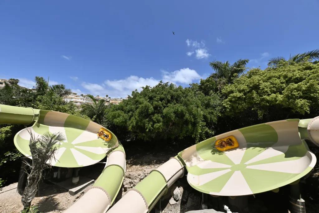 Siam Park Trees lining two waterparks which run next to each other. Both loop round in the same direction and have 2 people in yellow double rings. The photo is perfectly timed with both in the same place on the two slides.