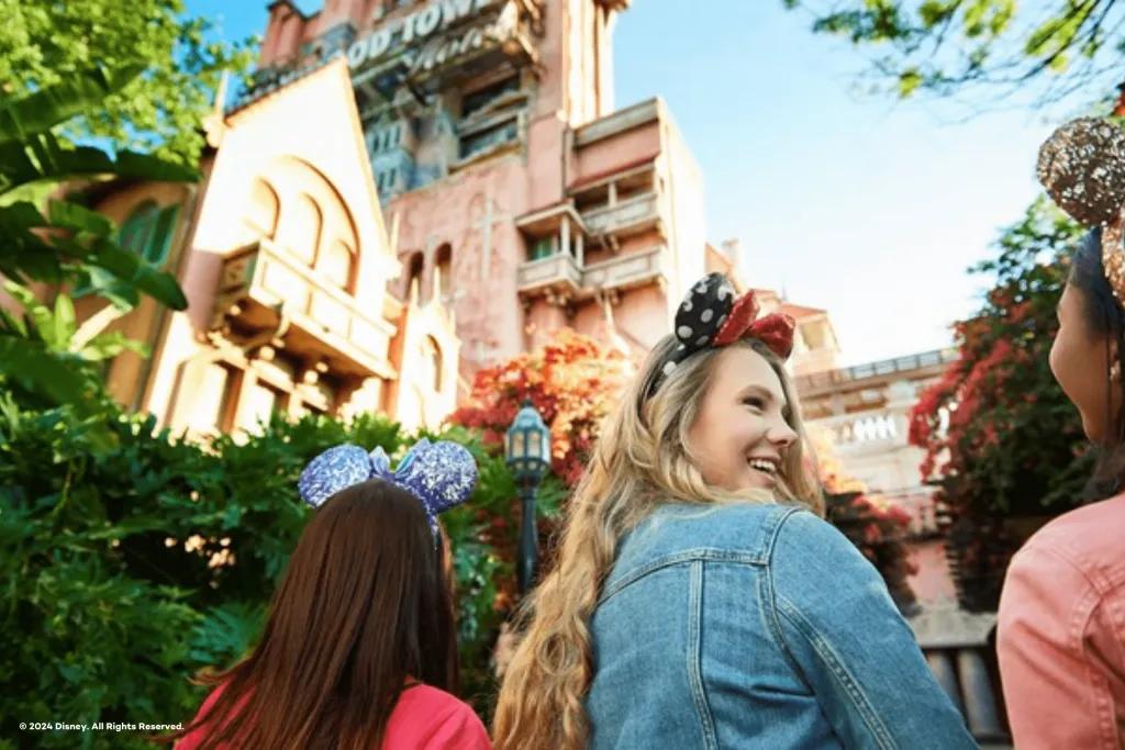 Disney's Hollywood Studios A group of young girls stood wearing mickey ears underneath a large dishevelled looking tower which is the Tower of Terror. One of the girls is turned to the others smiling.