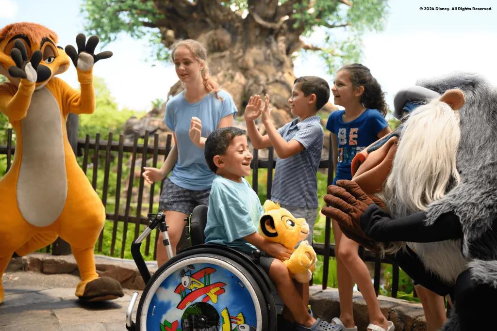 Disney's Animal Kingdom Theme Park A young boy in a wheelchair smiling at Rafiki, a cartoon monkey from the Lion King movie. There are three young kids behind them smiling looking at Timone, a cartoon meerkat from the Lion King. Behind there is a large tree with carvings of different animals on the large stump.