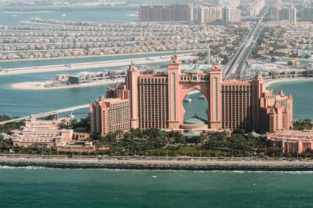Atlantis, The Palm Coral pink large hotel staggered levels and in the middle is a huge arch cut from the building. There is water surrounding this hotel and a long road connecting it to mainland Dubai.