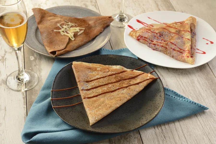 Creperie de Paris Three plates of crepes and a glass of champagne on the side. One crepe has chocolate sauce on it, one has strawberry sauce and the other has white chocolate shavings.