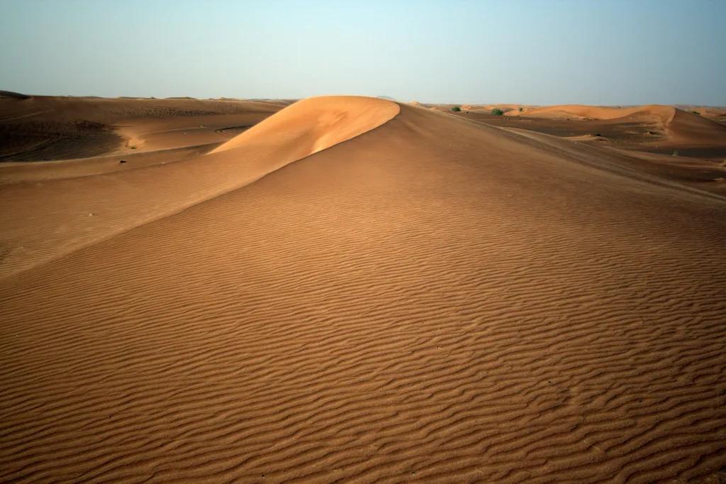 Arabian Desert A large sand dune in the middle of the desert with a clear blue sky above.