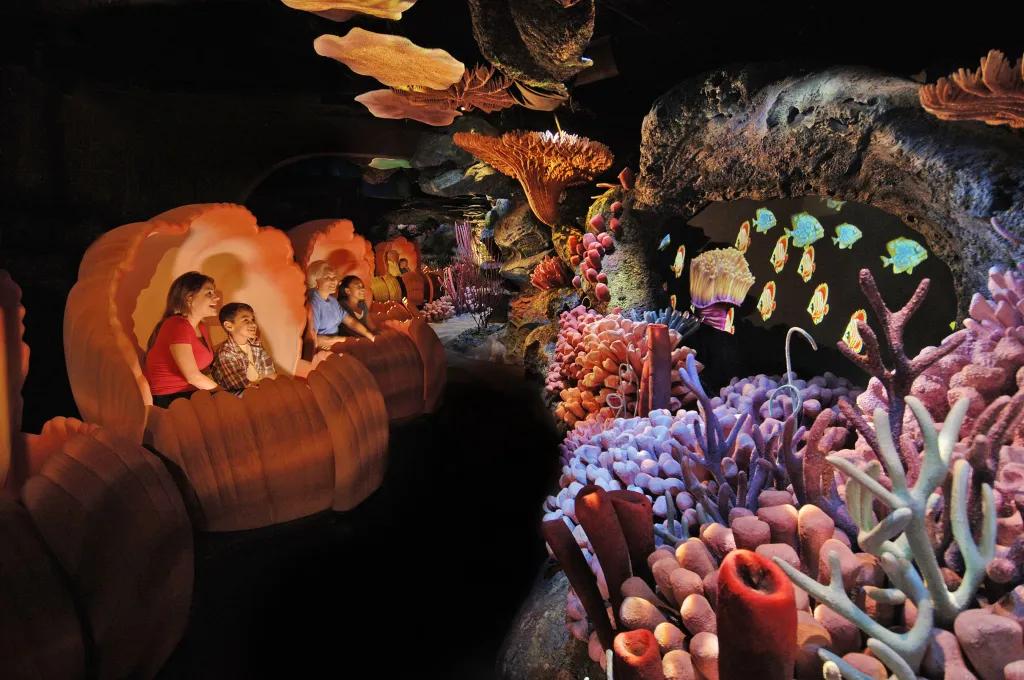Seas With Nemo and Friends Guests sat in clam shell ride vehicles looking over to coral reefs and projections of fish swimming.