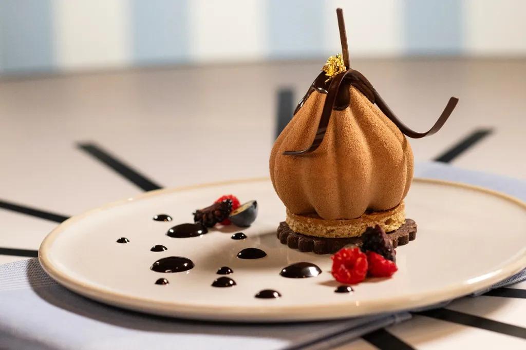 Trattoria del Porto Plate with mousse shaped like a tulip on a biscuit and chocolate shavings on. There are also drops of chocolate sauce around the plate.